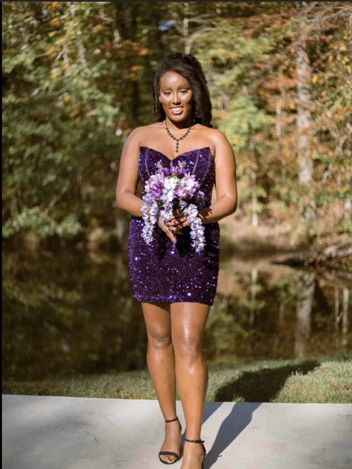 Person outdoors in a dark purple sparkly strapless short dress, holding a purple-and-white bouquet.